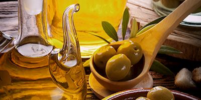 Traditional Olive Oil from Croatia in a dispenser, a spoon with three olives, and olive leaves.
