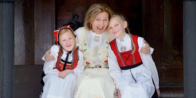 A woman hugging two little girls, dressed in traditional Norweigian garb.